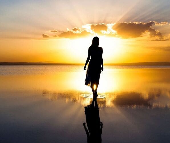 A woman walking on the beach at sunset.